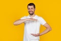 Young man with a beard in a white T-shirt gesturing with his hands showing a large and large size sign, a symbol of measure. Royalty Free Stock Photo