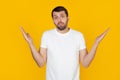 A young man with a beard in a white t-shirt is an ignorant and confused expression with raised arms and hands. Doubt concept. Royalty Free Stock Photo