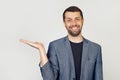 Young man with a beard in a white t-shirt smiling, cheerful presenting and pointing with his palm, looking at the camera. Stands Royalty Free Stock Photo