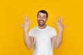 Young man with a beard in a white t-shirt smiling, showing the number ten with fingers on his hand, smiling confidently and Royalty Free Stock Photo