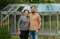 Smiling Young man with Aunt in front a glass greenhouse near summer house