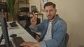 Young man with beard working on computer in modern office setting, pointing finger in focus, wearing denim shirt Royalty Free Stock Photo