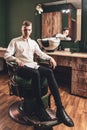 A young man with a beautiful hairstyle sits in a chair in a barbershop Royalty Free Stock Photo