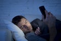 Young man in bed couch at home falling asleep late at night while using mobile phone in low light Royalty Free Stock Photo