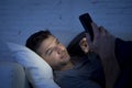 Young man in bed couch at home late at night texting on mobile phone in low light relaxed Royalty Free Stock Photo