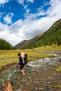 Young man with big backpack barefoot crossing river. Shoeless male backapcker in river. Karakol valley on trail to Ala Kul lake.