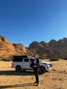 Young man with binoculars and car in desert. SUV off road auto vehicle.