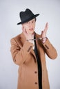 Young man in a black business suit and beige fashion coat with a stylish hat stands in police handcuffs on a white solid Studio ba Royalty Free Stock Photo