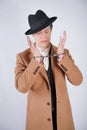 Young man in a black business suit and beige fashion coat with a stylish hat stands in police handcuffs on a white solid Studio ba Royalty Free Stock Photo