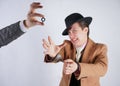 Young man in a black business suit and beige fashion coat with a stylish hat stands in police handcuffs on a white solid Studio ba Royalty Free Stock Photo