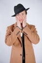 Young man in a black business suit and beige fashion coat with a stylish hat stands in police handcuffs on a white solid Studio ba Royalty Free Stock Photo