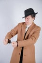 Young man in a black business suit and beige fashion coat with a stylish hat stands in police handcuffs on a white solid Studio ba Royalty Free Stock Photo