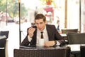 A young man in a black business suit, white shirt and tie sits in a city street cafe at a table and enjoys his cappuccino with foa Royalty Free Stock Photo