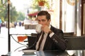 A young man in a black business suit, white shirt and tie is sitting in a city street cafe at a table and enjoying a Cup of coffee Royalty Free Stock Photo