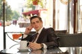 A young man in a black business suit, white shirt and tie is sitting in a city street cafe at a table and enjoying a Cup of coffee Royalty Free Stock Photo