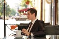 A young man in a black business suit, white shirt and tie is sitting in a city street cafe at a table and enjoying a Cup of coffee Royalty Free Stock Photo