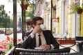 A young man in a black business suit, white shirt and tie is sitting in a city street cafe at a table and enjoying a Cup of coffee Royalty Free Stock Photo