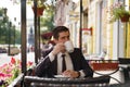 A young man in a black business suit, white shirt and tie is sitting in a city street cafe at a table and enjoying a Cup of coffee Royalty Free Stock Photo