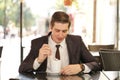 A young man in a black business suit, white shirt and tie sits in a city street cafe at a table and enjoys his cappuccino with foa Royalty Free Stock Photo