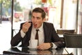 A young man in a black business suit, white shirt and tie sits in a city street cafe at a table and enjoys his cappuccino with foa Royalty Free Stock Photo