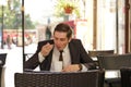 A young man in a black business suit, white shirt and tie sits in a city street cafe at a table and enjoys his cappuccino with foa Royalty Free Stock Photo