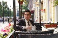 A young man in a black business suit, white shirt and tie is sitting in a city street cafe at a table and enjoying a Cup of coffee Royalty Free Stock Photo