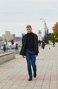 A young man in a black jacket is walking along the city embankment. Lighthouse in the background in blur. Selective Royalty Free Stock Photo