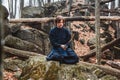 Young man in black kimono with a sword meditates and concentrates on rocks and forest background. Place for text or advertising