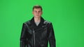 Young man in black leather jacket going and looking forward against a green background. Slow motion.