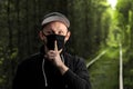 Young man in black protective antiviral mask with a finger to his lips in the summer park. The guy is resting outdoors in a mask Royalty Free Stock Photo