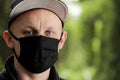 Young man in black protective antiviral mask in the summer park. The guy is resting outdoors on a sunny summer day in a mask made Royalty Free Stock Photo