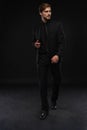 Young man in black suit full body portrait against black background. Royalty Free Stock Photo