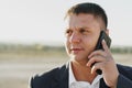 Young man in a black suit standing outdoors and talking on the phone close up Royalty Free Stock Photo