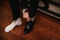 Young man in a black suit and white socks wears his black shoes on a dark background Royalty Free Stock Photo