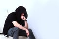 A young man in a black tracksuit sits brooding in a chair. The hood is pulled down over his face. Unrecognizable photo. Copy of