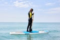 Young man in black wetsuit with paddle on sub board floats on water in ocean Royalty Free Stock Photo