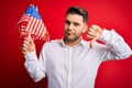 Young man with blue eyes holding flag of united states of america over red isolated background with angry face, negative sign Royalty Free Stock Photo