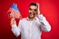 Young man with blue eyes holding flag of united states of america over red isolated background with happy face smiling doing ok Royalty Free Stock Photo