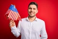 Young man with blue eyes holding flag of united states of america over red isolated background with a happy face standing and Royalty Free Stock Photo