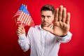 Young man with blue eyes holding flag of united states of america over red isolated background with open hand doing stop sign with Royalty Free Stock Photo