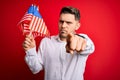 Young man with blue eyes holding flag of united states of america over red isolated background pointing with finger to the camera Royalty Free Stock Photo