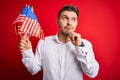Young man with blue eyes holding flag of united states of america over red isolated background serious face thinking about Royalty Free Stock Photo