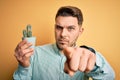 Young man with blue eyes holding fresh cactus plant pot over yellow background pointing with finger to the camera and to you, hand