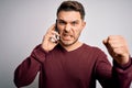 Young man with blue eyes speaking on the phone having a conversation on smartphone annoyed and frustrated shouting with anger, Royalty Free Stock Photo