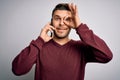 Young man with blue eyes speaking on the phone having a conversation on smartphone with happy face smiling doing ok sign with hand Royalty Free Stock Photo