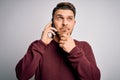 Young man with blue eyes speaking on the phone having a conversation on smartphone serious face thinking about question, very Royalty Free Stock Photo