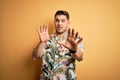 Young man with blue eyes on vacation wearing floral summer shirt over yellow background afraid and terrified with fear expression Royalty Free Stock Photo