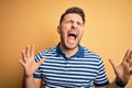 Young man with blue eyes wearing casual striped t-shirt over yellow background crazy and mad shouting and yelling with aggressive Royalty Free Stock Photo