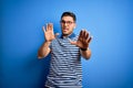 Young man with blue eyes wearing glasses and casual striped t-shirt over blue background afraid and terrified with fear expression Royalty Free Stock Photo