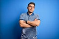 Young man with blue eyes wearing glasses and casual striped t-shirt over blue background smiling looking to the side and staring Royalty Free Stock Photo